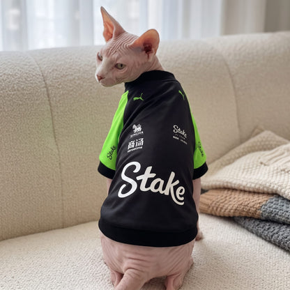 Sphynx cat on sofa wearing Stake F1 2025 pet shirt back view with white Stake logo
